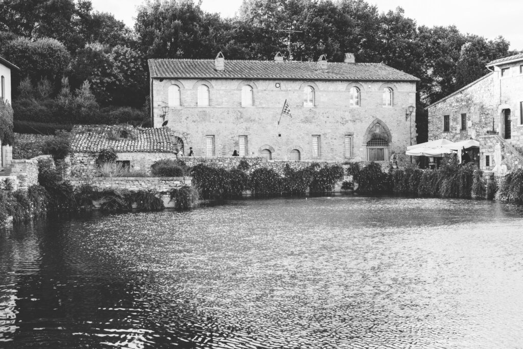 The thermal pool of Piazza delle Sorgenti in Bagno Vignoni with the stone buildings behind it, in black and white