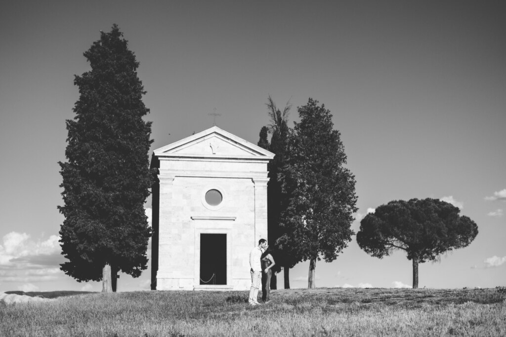 Engaged couple in front of the Chapel of Vitaleta between its cypresses, Val d'Orcia, in black and white
