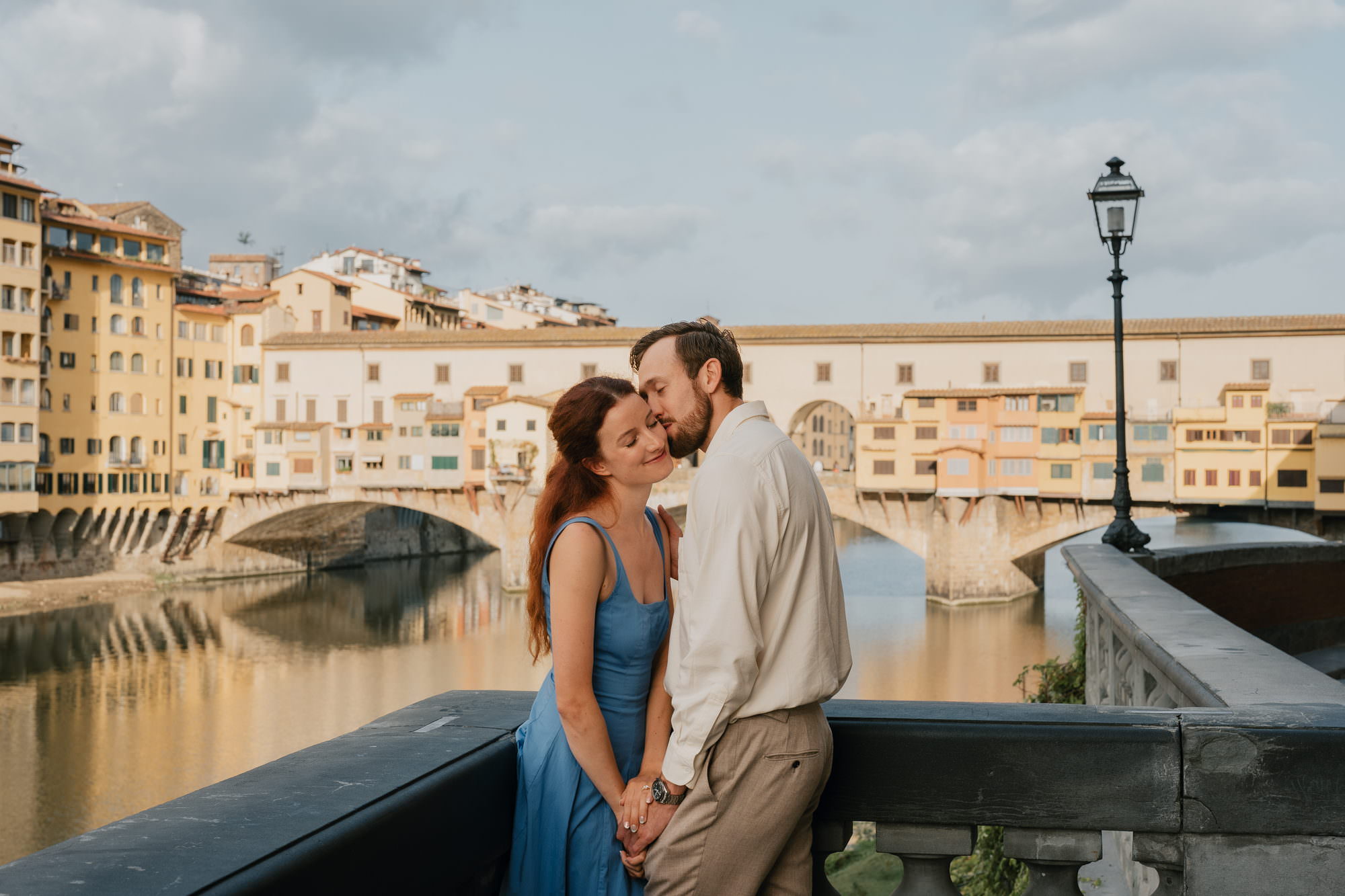 Couple embracing on the Arno embankment in Florence, with the Ponte Vecchio behind them