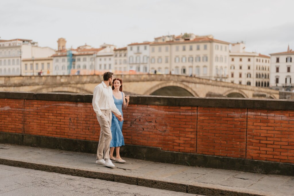Couple standing on the Arno embankment in Florence with the Oltrarno houses behind them