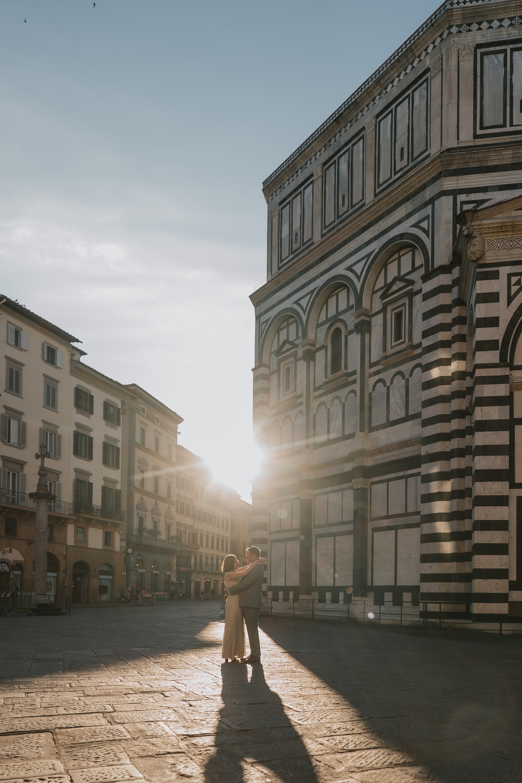 Couple embracing by the Baptistery of Florence at sunrise, with long shadows on the square