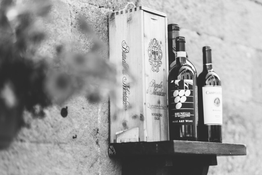 Bottles of Brunello di Montalcino on a wooden shelf against a stone wall in Pienza