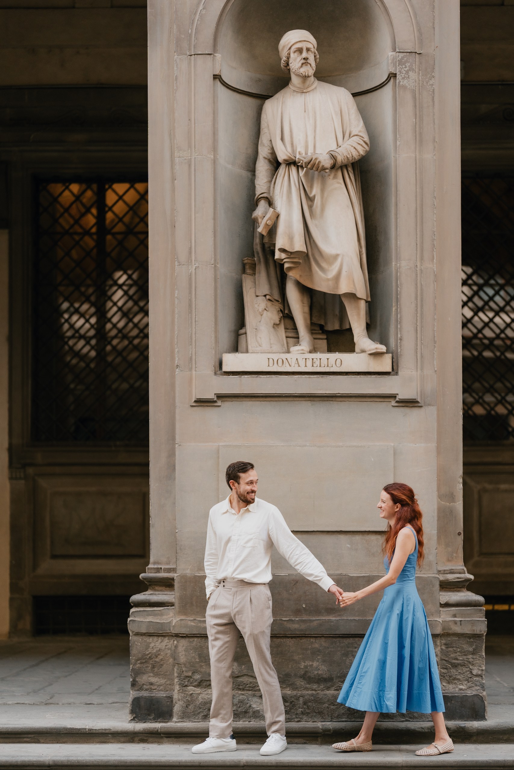 Couple holding hands below a statue in the portico of the Uffizi, Florence