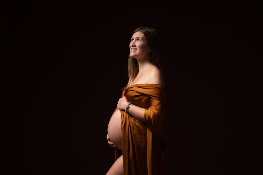 Servizio fotografico gravidanza in studio: futura mamma nel telo color ruggine su fondo scuro