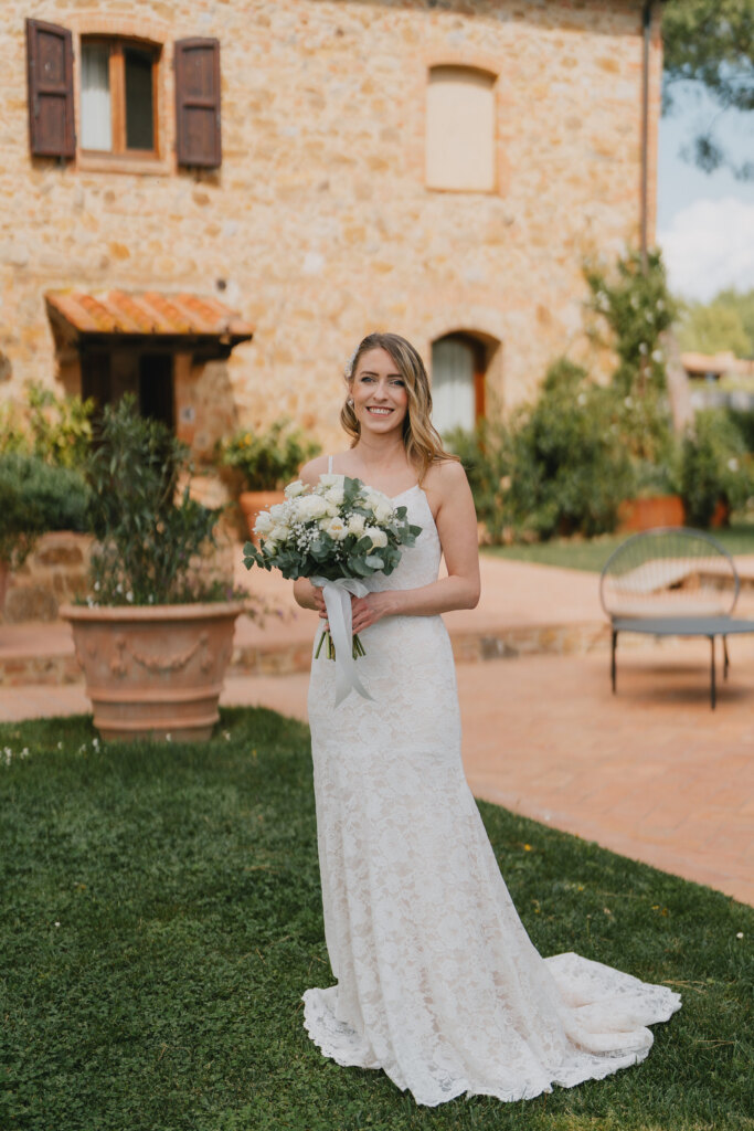 Bride holding a white bouquet in front of the stone farmhouse at Mormoraia