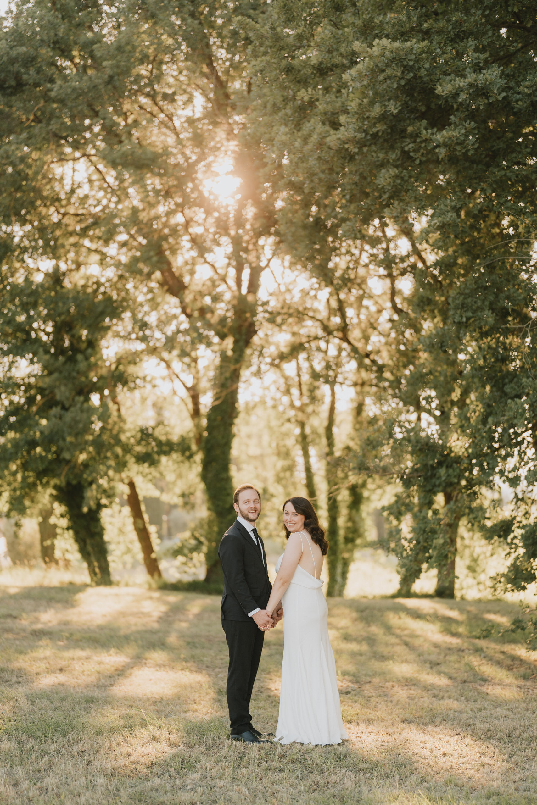 Bride and groom under the trees, the afternoon sun through the leaves