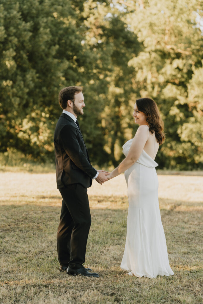 Bride and groom holding hands on a grassy path under tall trees at La Sovana