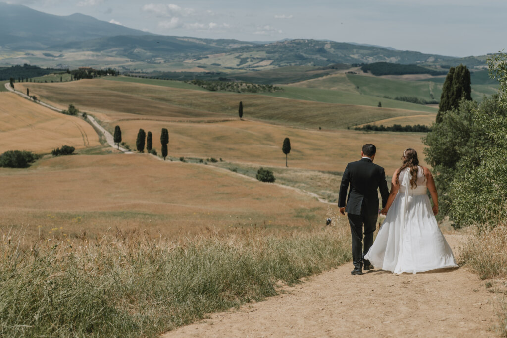 Newlyweds walking hand in hand down a dirt road among the cypresses of the Val d'Orcia