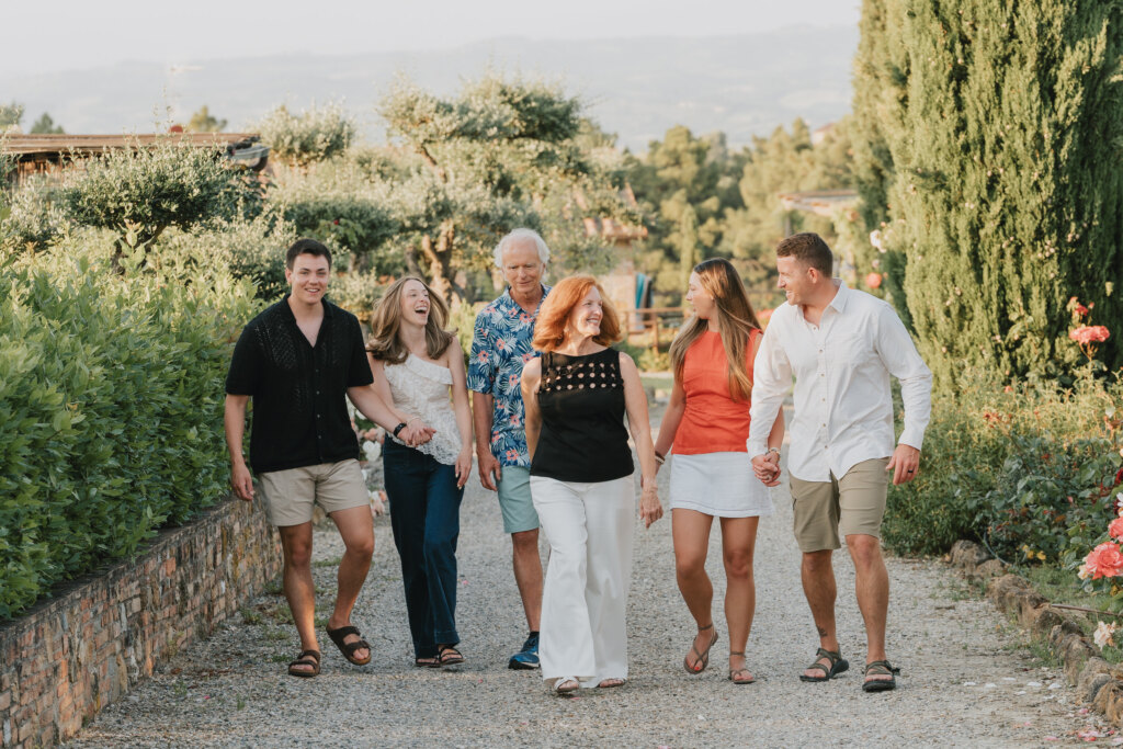 Famiglia allargata che cammina mano nella mano lungo un vialetto di ghiaia tra i cipressi in Toscana