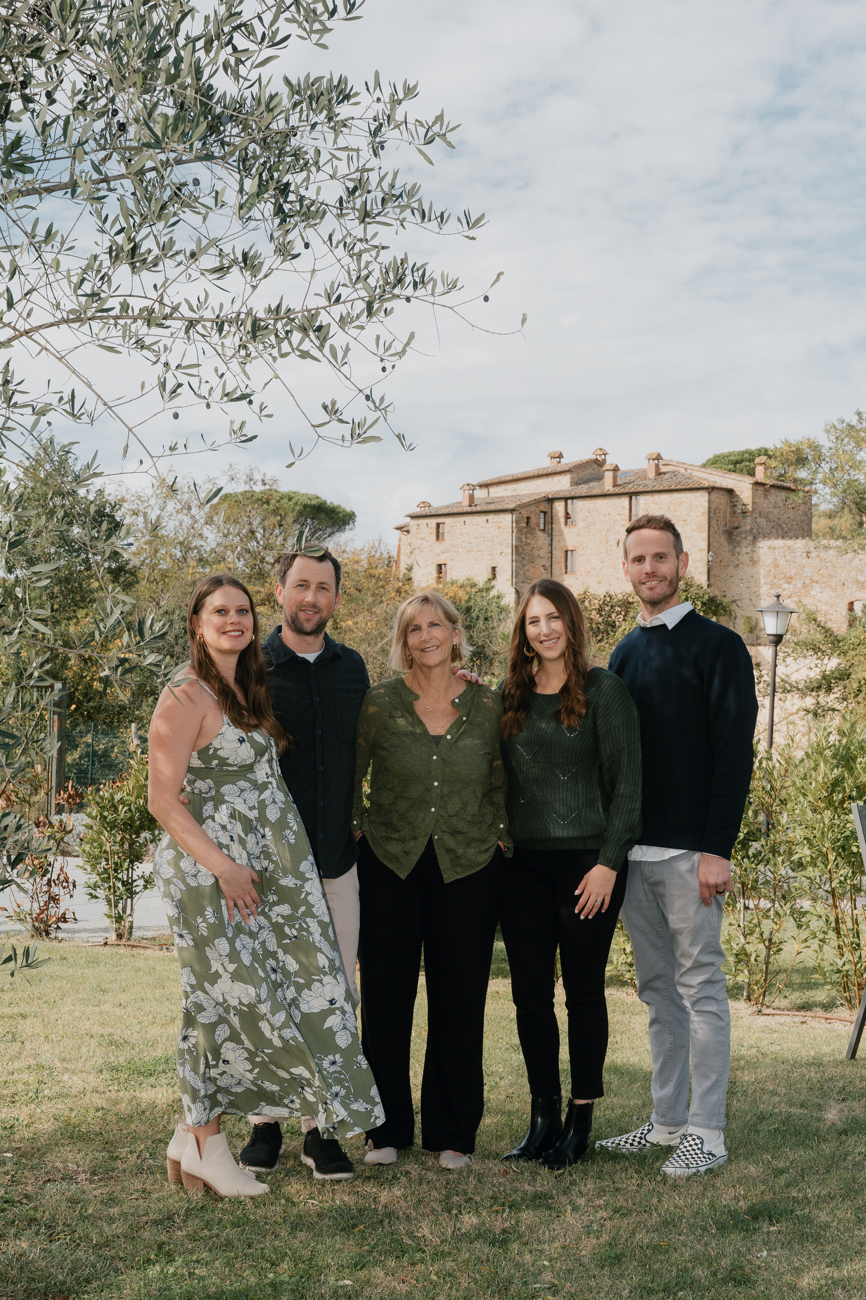 Madre con i figli adulti e i loro compagni in piedi nel giardino di una villa vicino a Siena, con la villa in pietra sullo sfondo