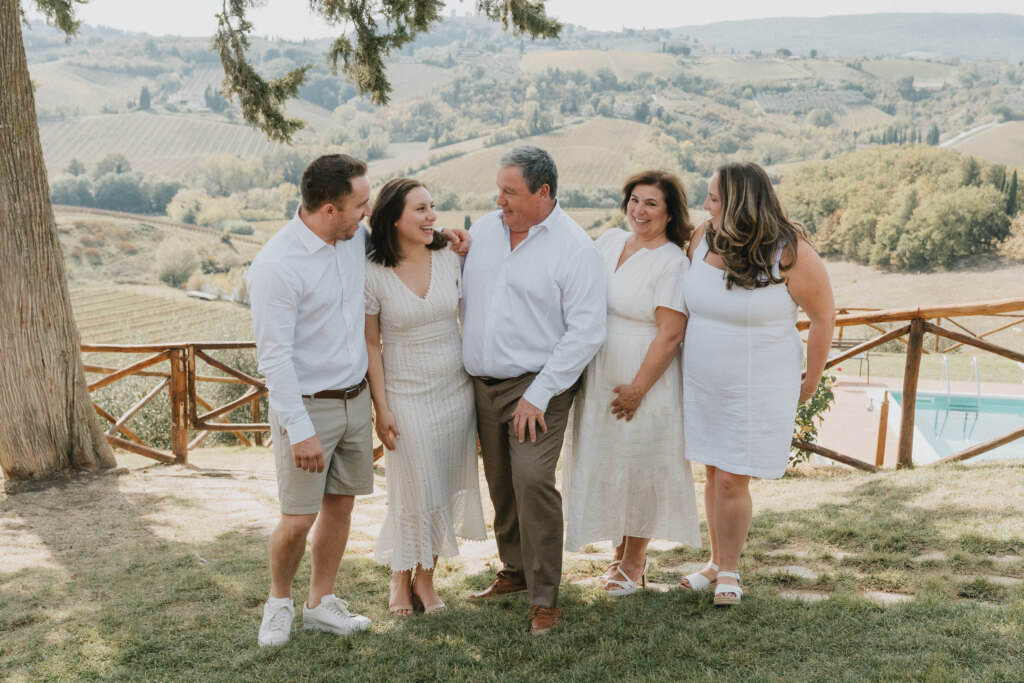 Genitori con i figli adulti che ridono insieme nella campagna di San Gimignano, con vigneti e colline sullo sfondo