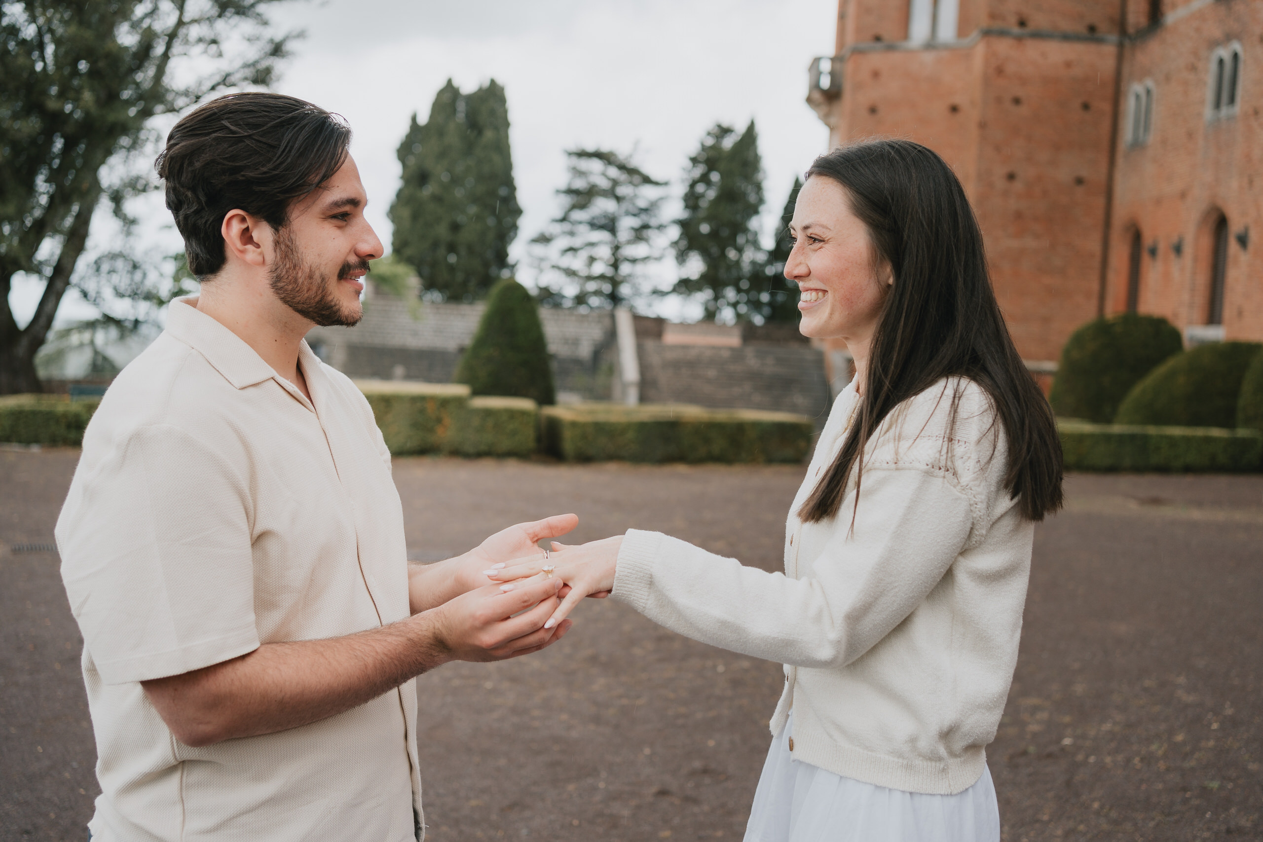 Couple holding hands and laughing after the proposal in front of Castello di Brolio, Chianti