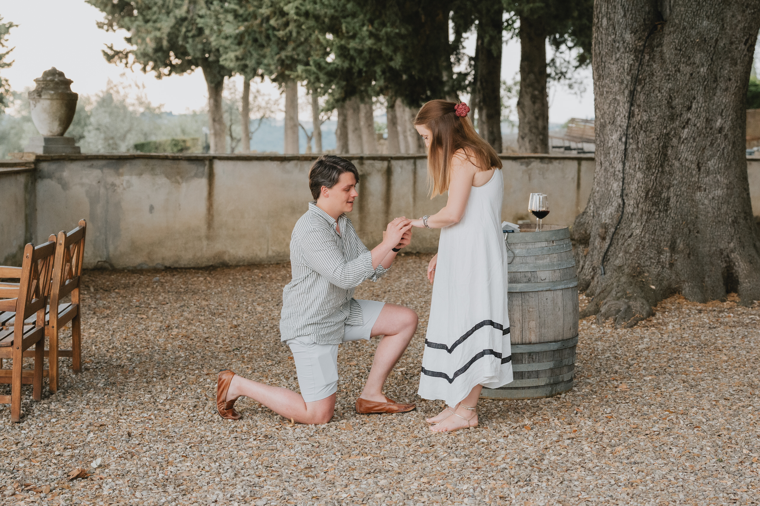 Proposal under the trees at Cinciano in Chianti, a wine barrel and glasses beside the couple