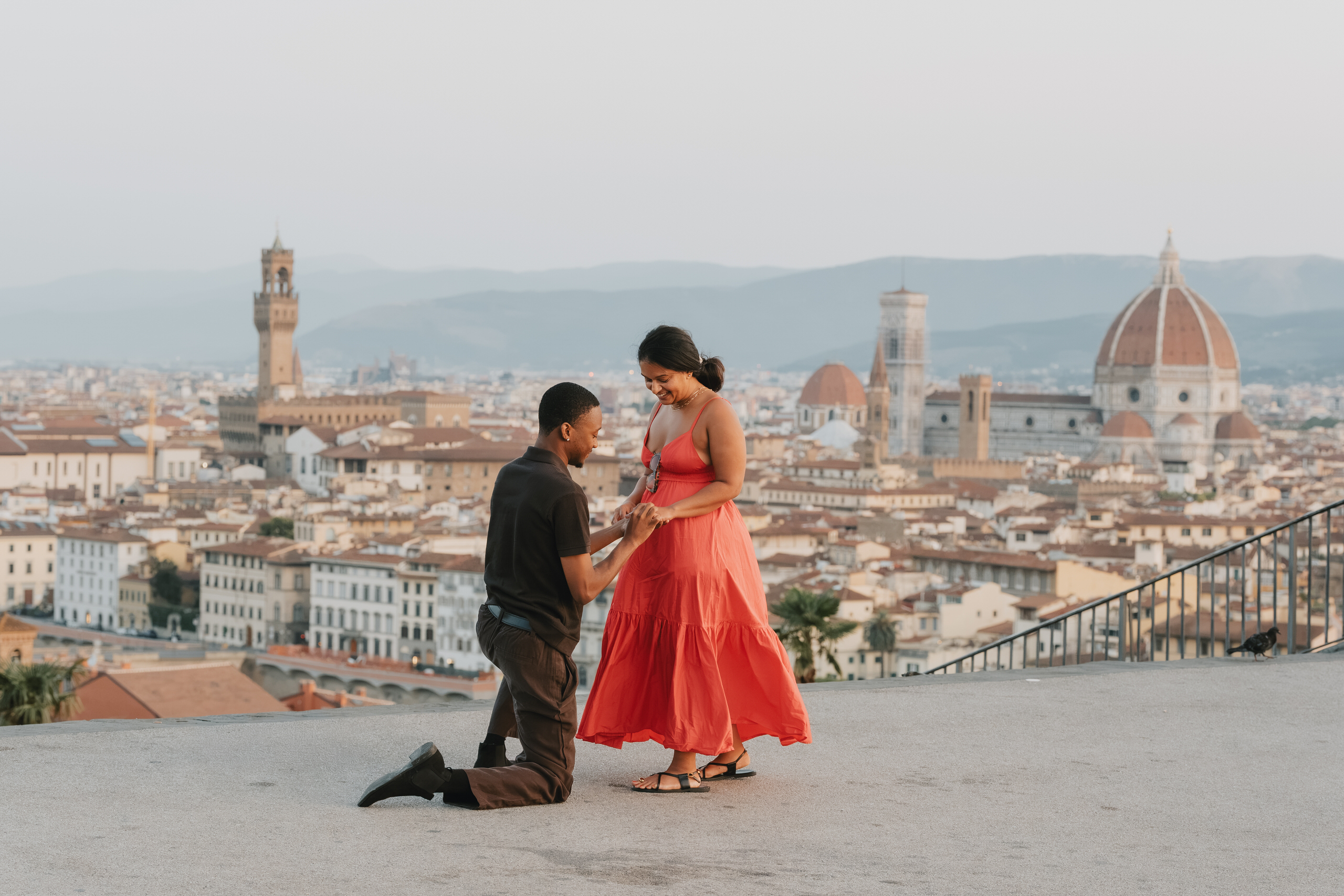 Proposal above Florence at golden hour, she in a red dress, the Duomo and Palazzo Vecchio behind