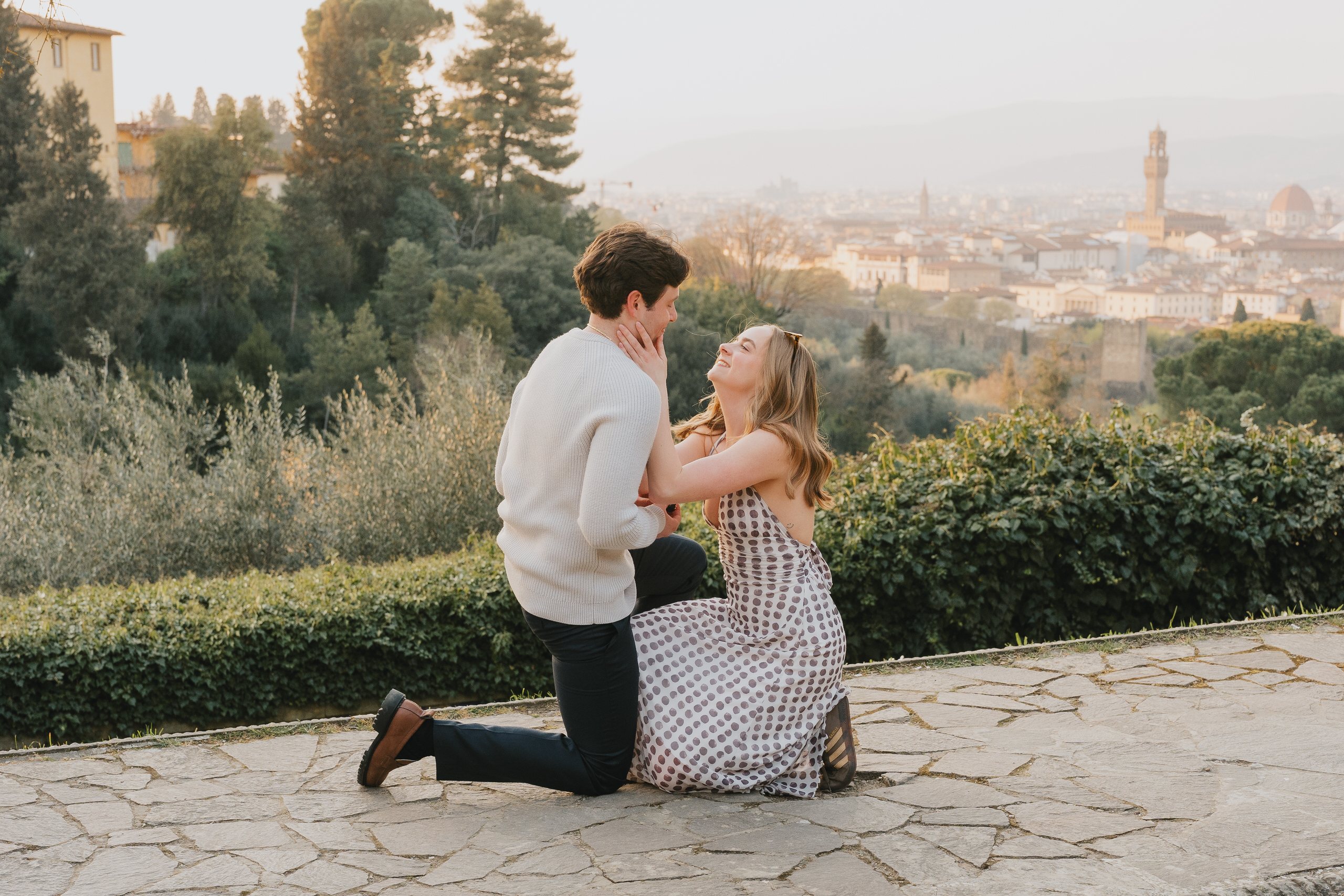 He kneels as she leans in to kiss him, proposal on a terrace above Florence