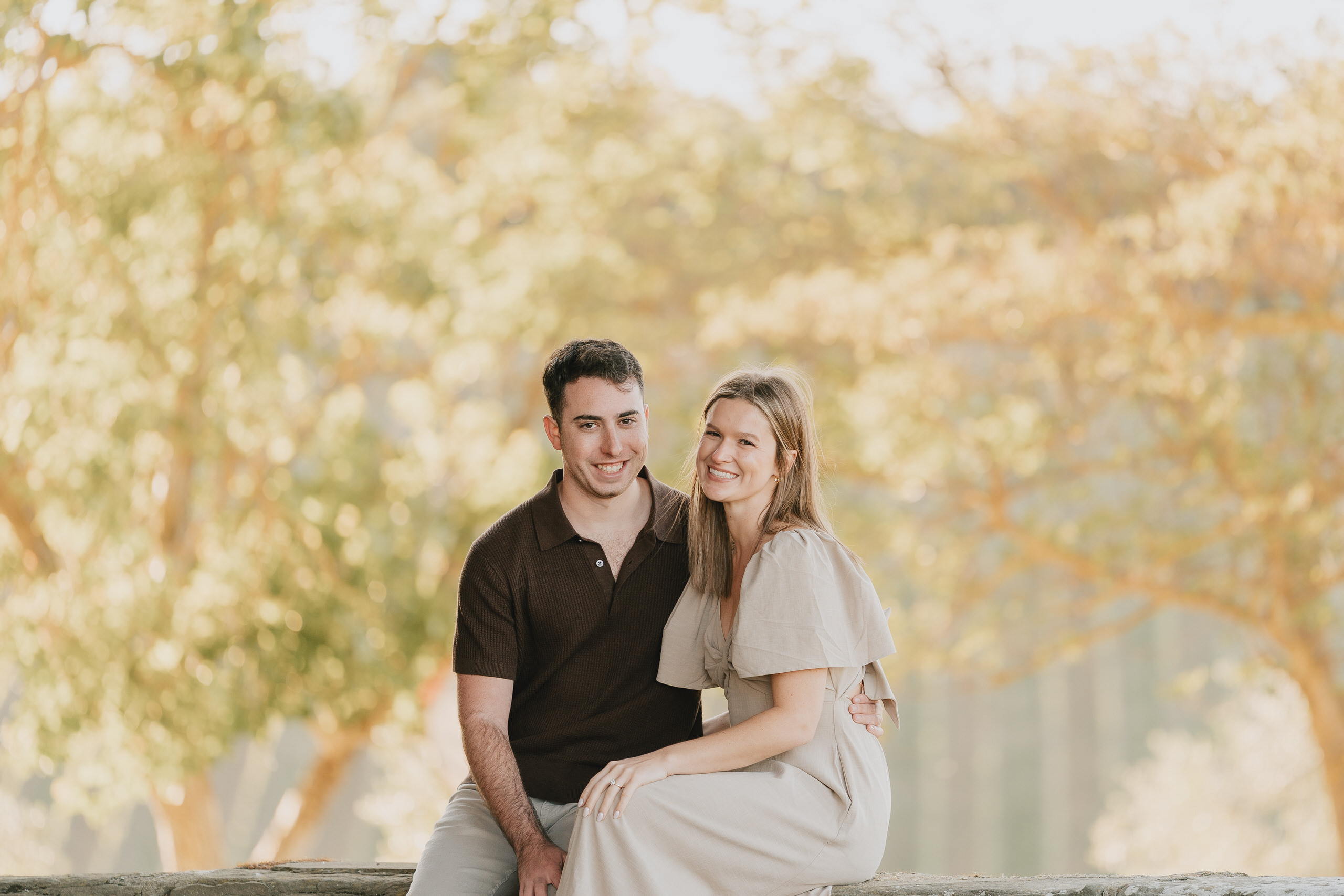 Couple sitting on a stone wall under the trees after the proposal in Florence