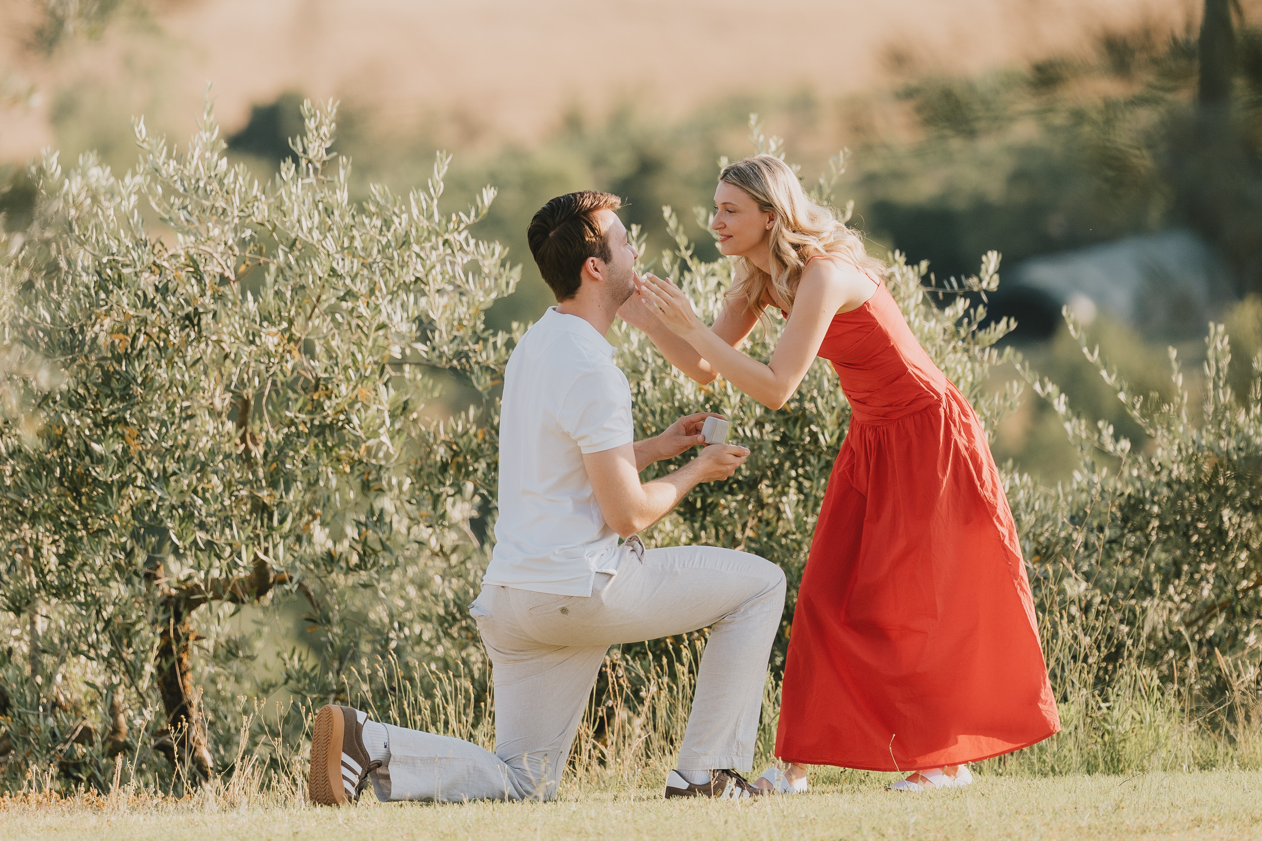 She kisses him as he kneels among olive trees at La Mormoraia, San Gimignano