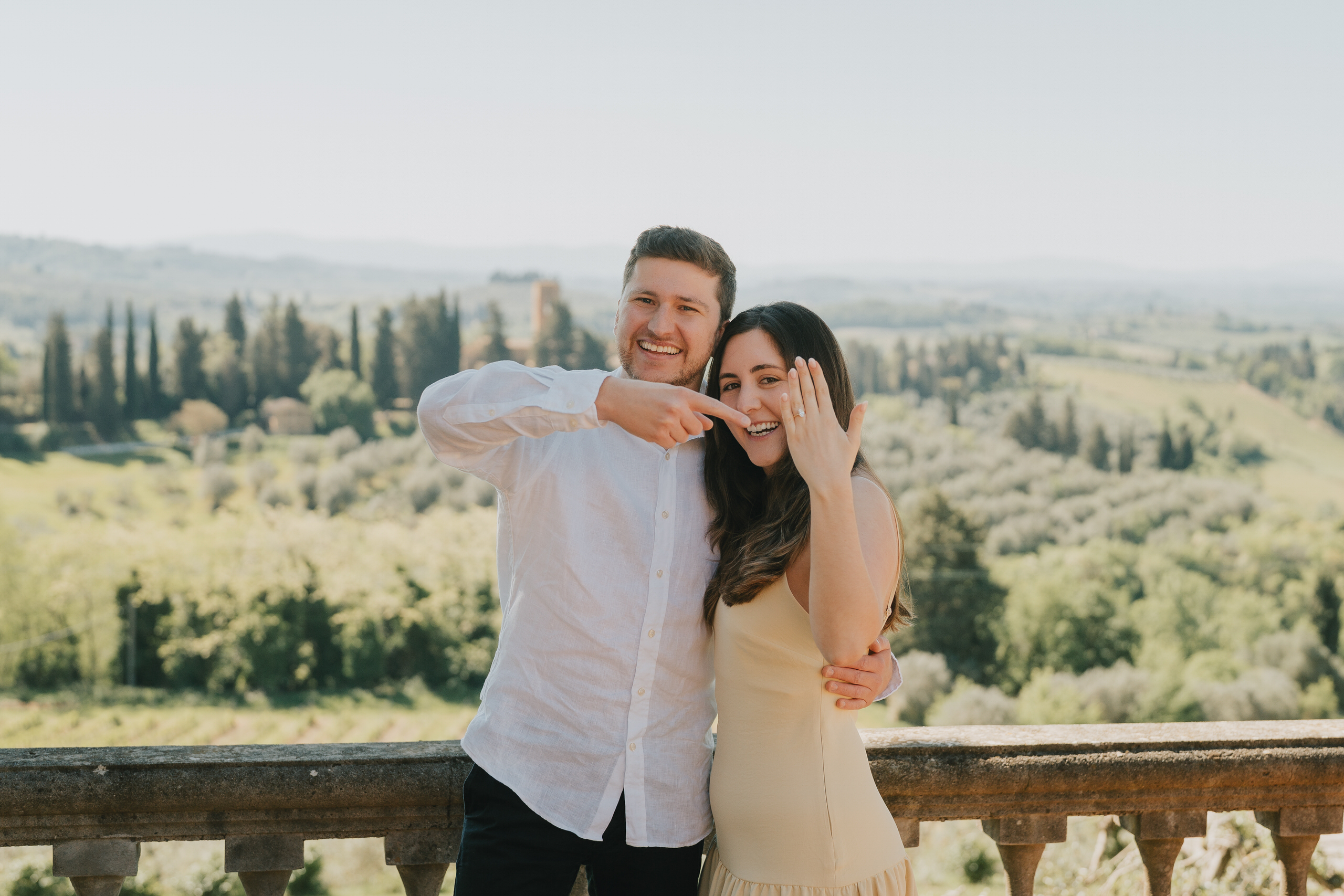 Couple showing the ring on the terrace of Villa Il Pozzo, countryside behind