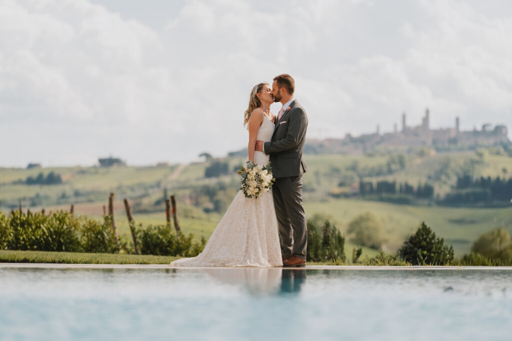 San Gimignano elopement: bride and groom kissing by the pool with the towers on the horizon