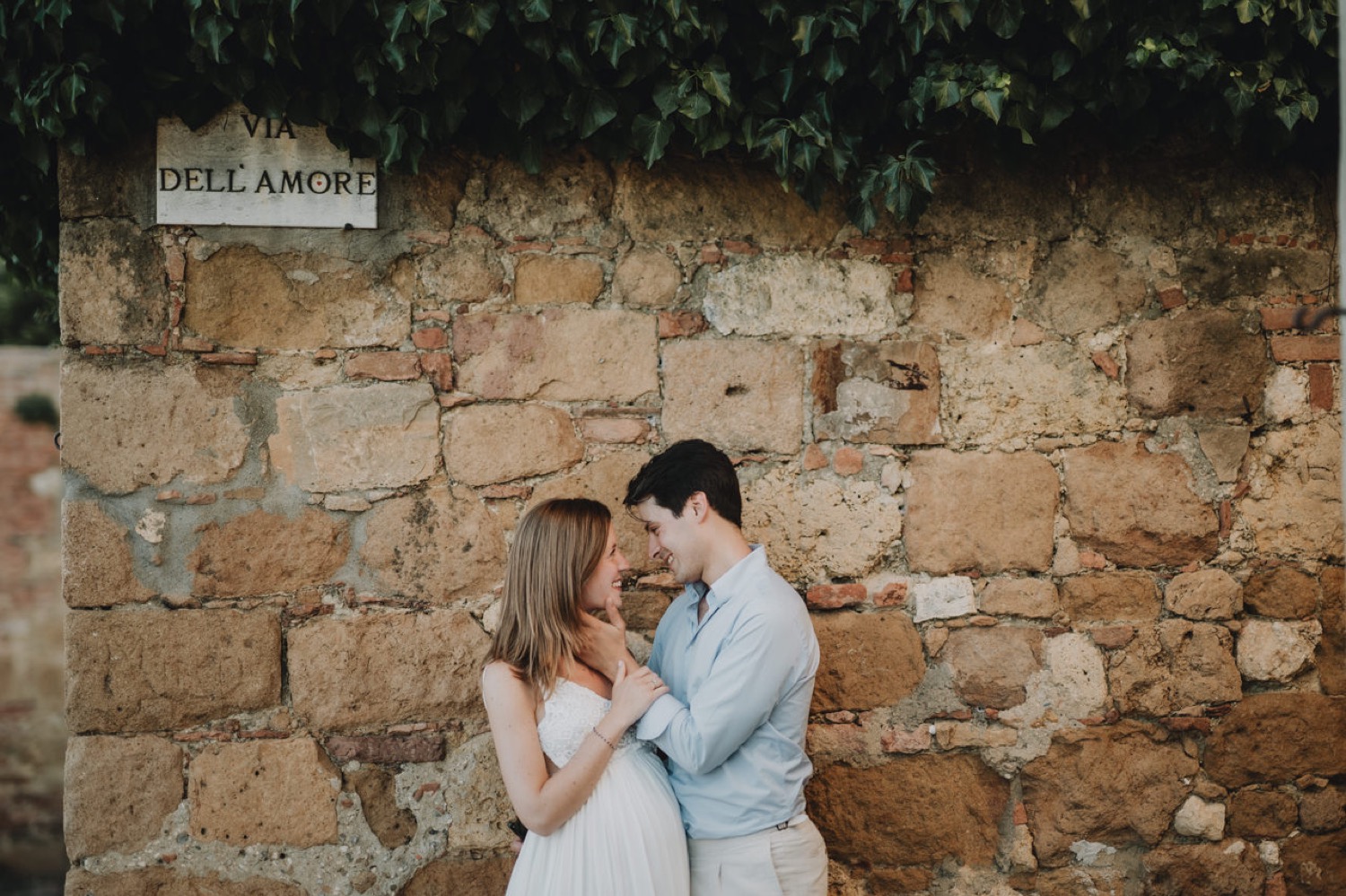 Expecting couple kissing against a stone wall in Pienza