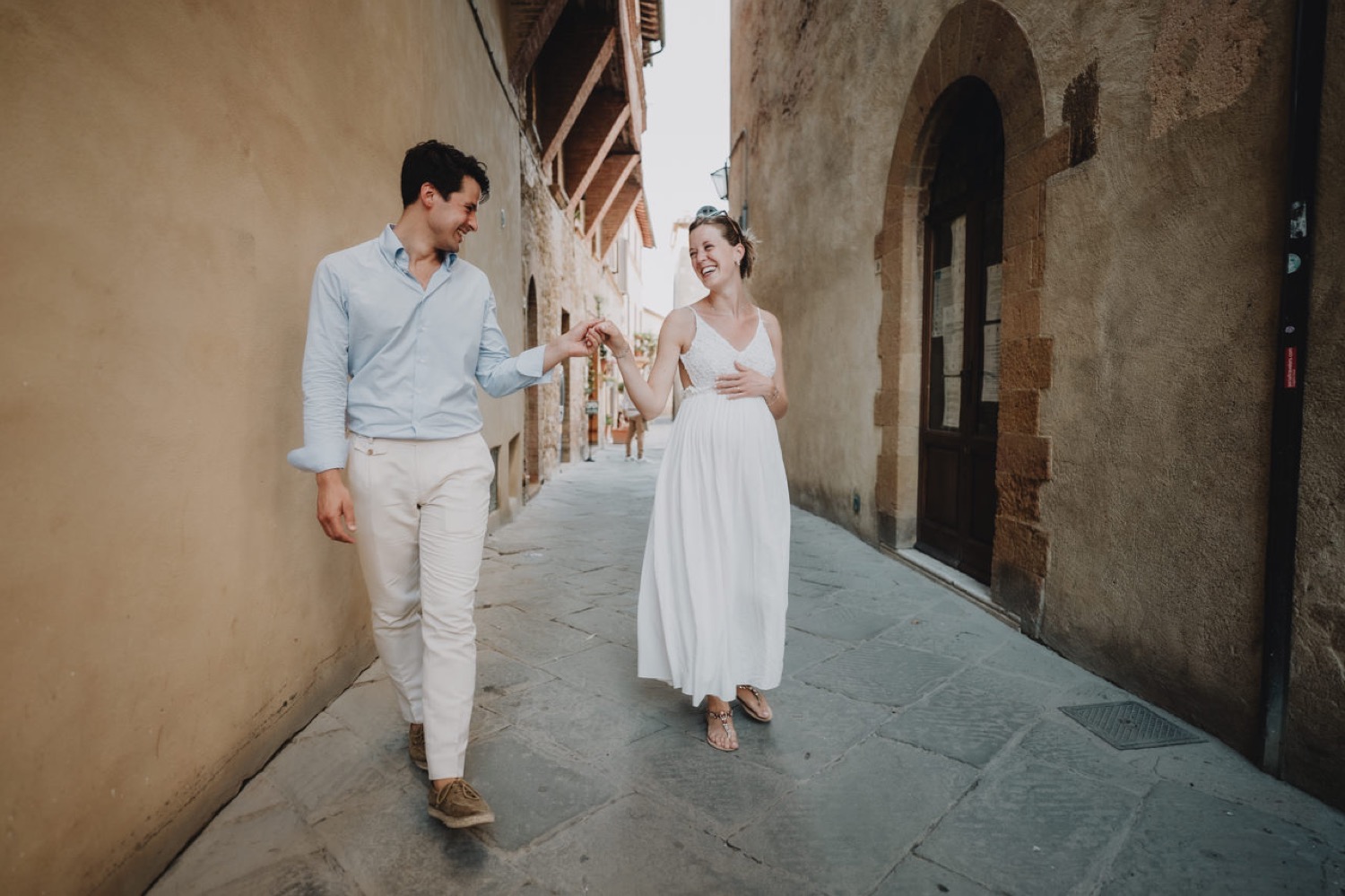 Expecting couple walking hand in hand through a lane in Pienza