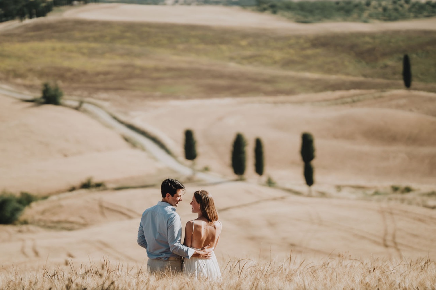 Couple walking on a white road lined with cypresses