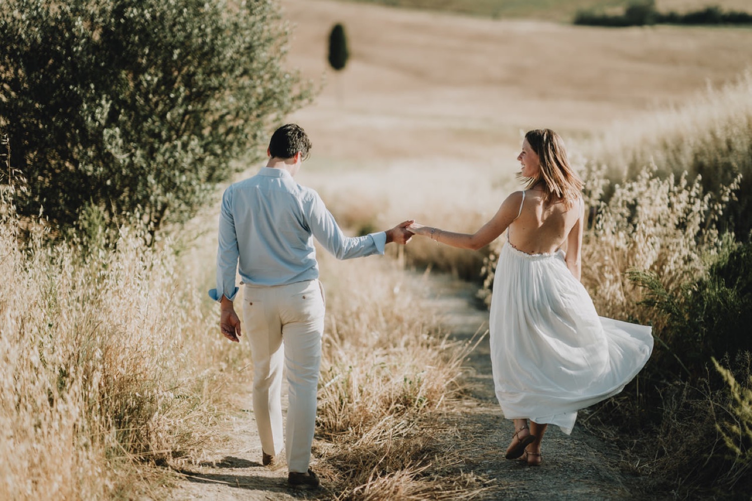 Couple holding hands next to an olive tree in the fields