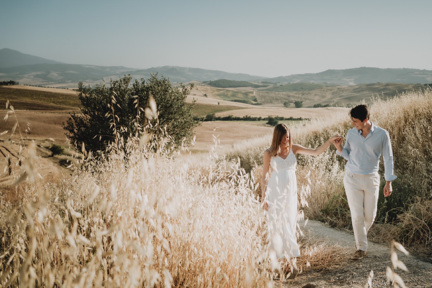 Expecting couple walking among olive trees and dry grass