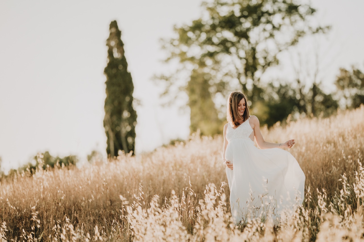 Mother-to-be in white among the grasses, a cypress behind her
