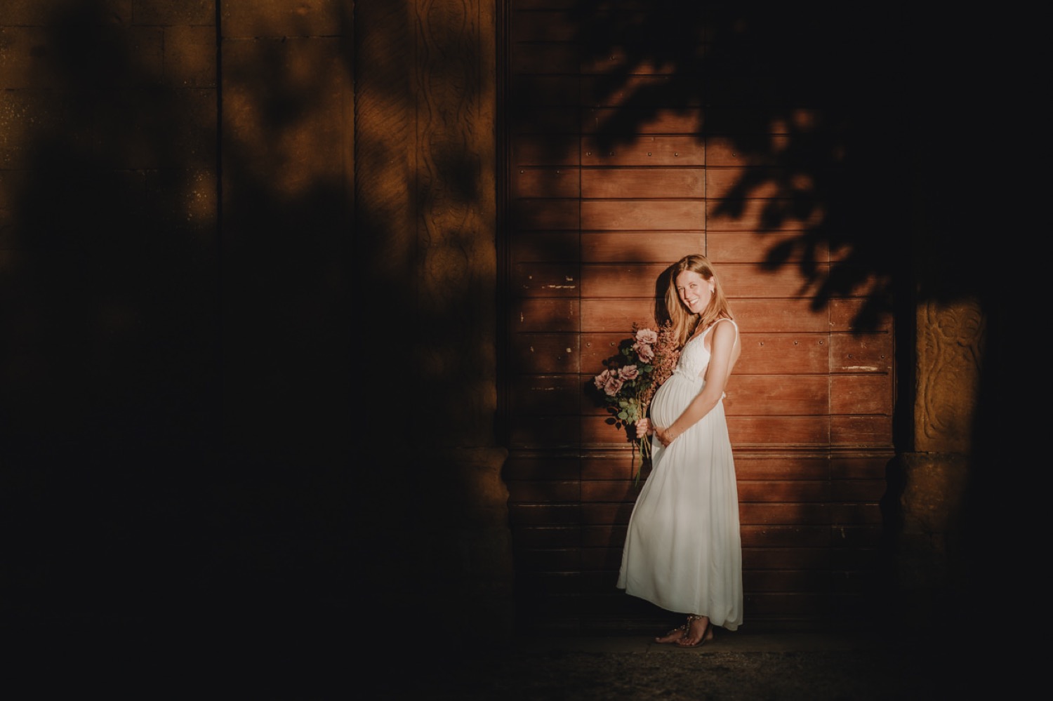 Pregnant woman in white in the shade of a stone wall