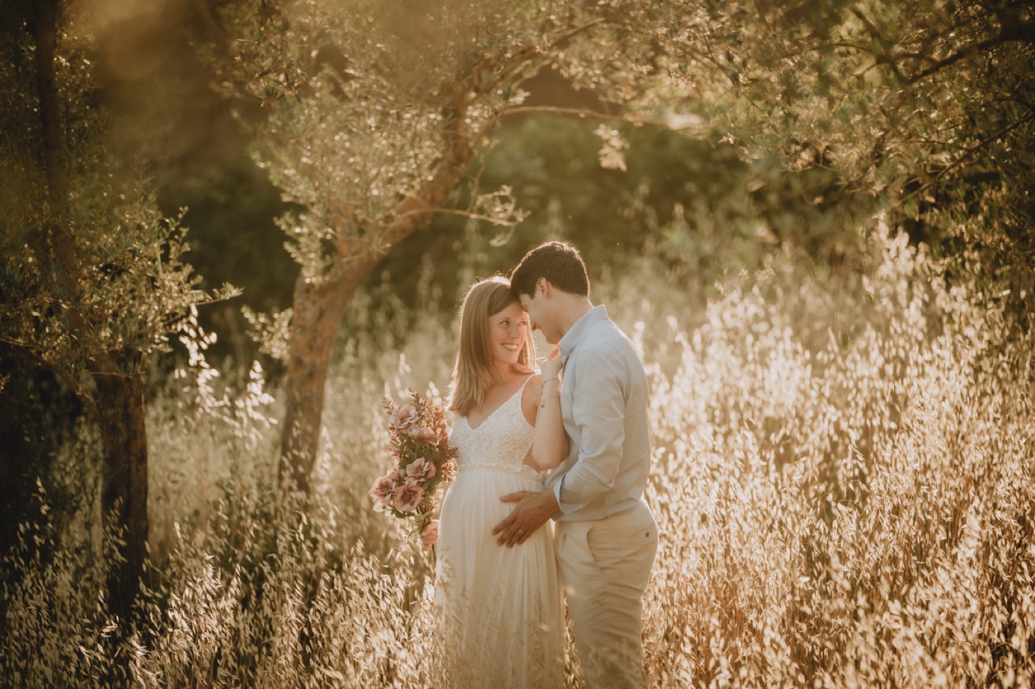 Couple embracing in the backlit grass among the trees
