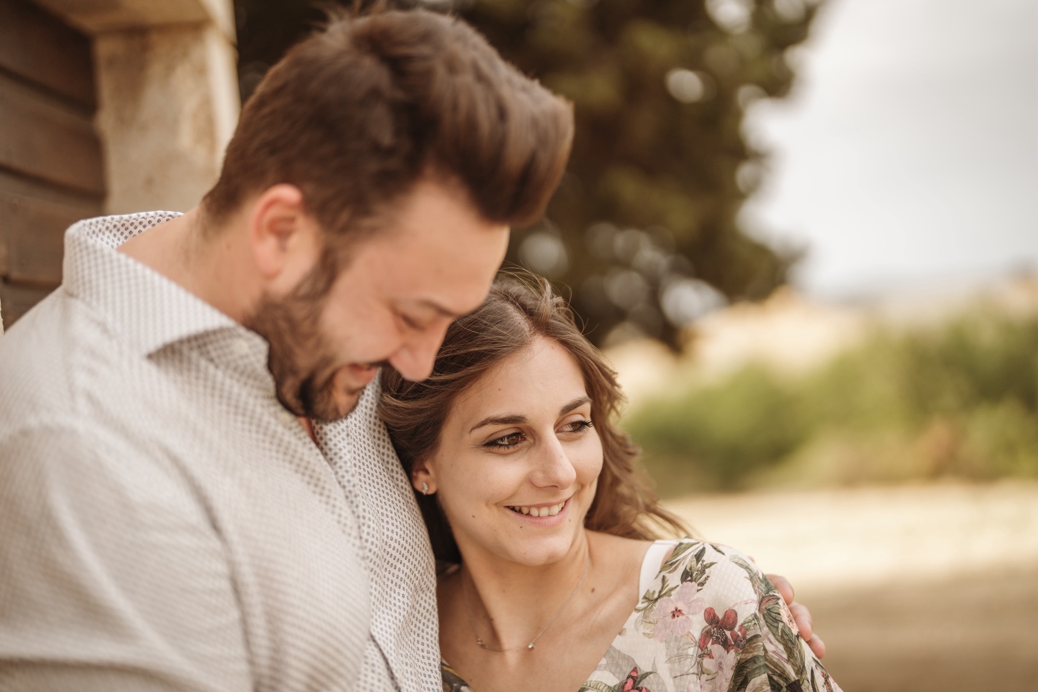 Lui e lei abbracciati e sorridenti accanto a un muro di pietra
