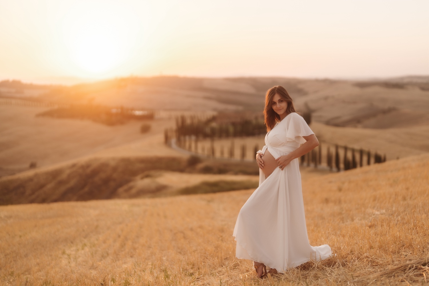 Futura mamma in abito bianco sulle colline al tramonto