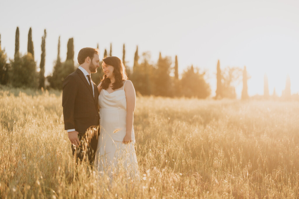 Valdichiana elopement: bride and groom in golden grass with a row of cypresses behind them