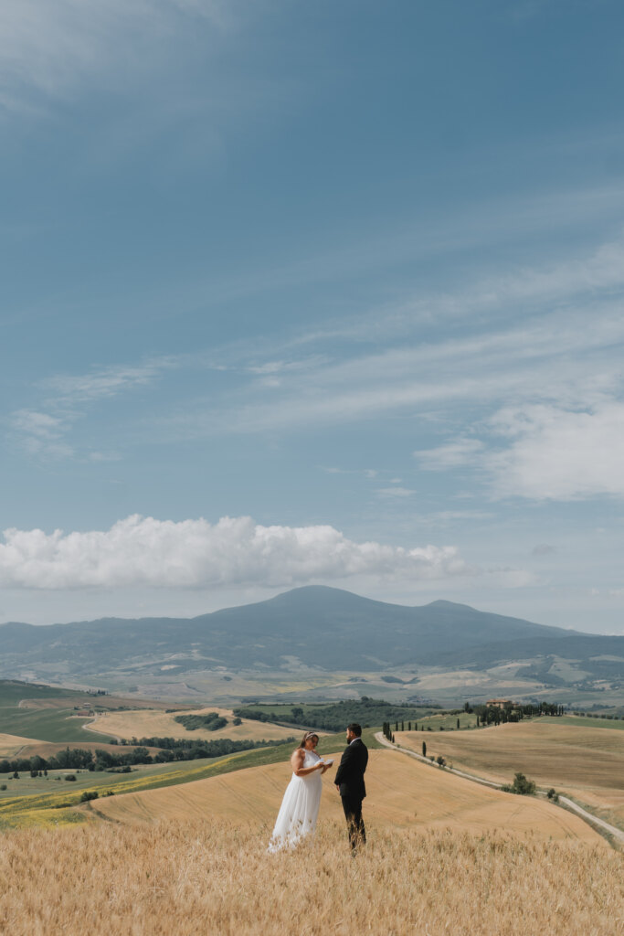 Bride and groom reading their vows in a wheat field, Monte Amiata on the horizon